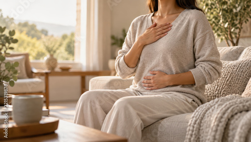 Nervous system regulation at home with calm breathing and gentle hand on chest and belly, woman sitting on sofa