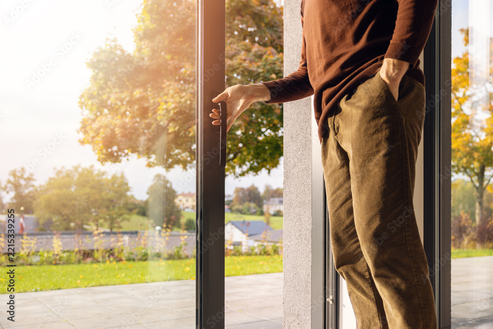 Fototapeta premium Man opening large aluminum sliding glass patio door to a backyard garden