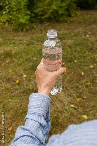 Obraz na plátně Person holding a reusable-style plastic water bottle on a woodland trail, conveying refreshment, hiking, fitness, and connection with nature