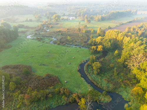 Aerial view of the winding Rawka River surrounded by meadows and autumn woodland near Bolimów, Poland