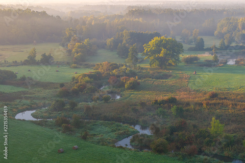 Aerial view of the meandering Rawka River flowing through autumn meadows and woodland near Bolimów, Poland