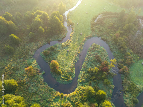 Aerial view of a winding Rawka River meander surrounded by autumn vegetation and morning mist near Bolimów, Poland