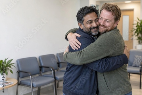 Two emotional men friends hugging in hospital waiting room, support with good news, friendship, relief, joy