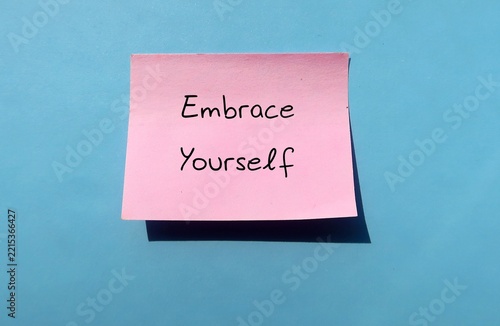 Pink paper on blue wall written Embrace Yourself - means to fully accept, love and value who you are, including your strengths, flaws, and uniqueness without harsh judgment
