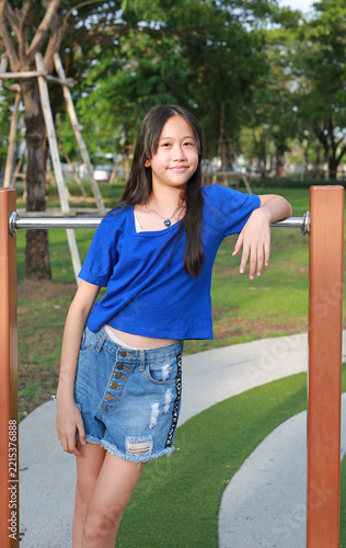 Portrait of young girl in blue shirt is leaning against the playground bars, while looking at camera.
