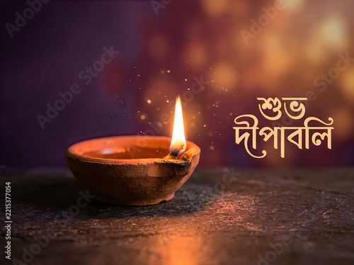 Traditional clay diya lamp with glowing flame for diwali festival celebration, with bengali text shuvo deepabali on a dark bokeh background