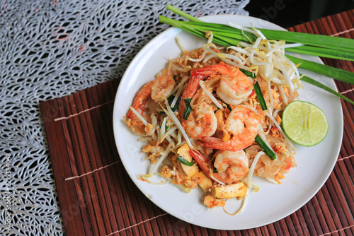 Delicious Pad Thai stir-fried rice noodles served with fresh prawns, bean sprouts, lime, and chives on a white plate.