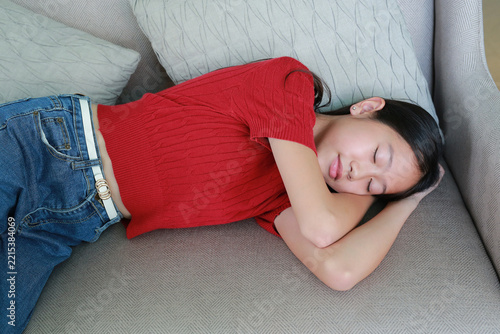 Young Asian girl in red shirt sleeping peacefully on a comfortable sofa at home.