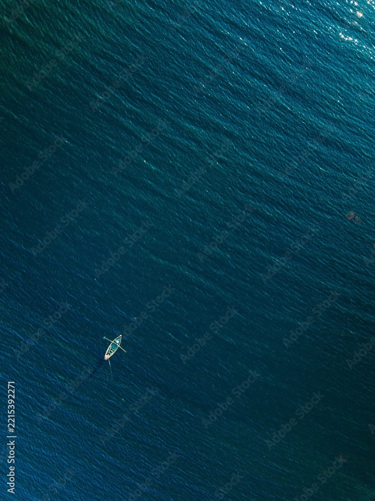 Fototapeta premium Single white kayak paddling through deep blue ocean waves under clear sunlight reflections in...