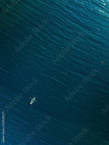 Single white kayak paddling through deep blue ocean waves under clear sunlight reflections in...