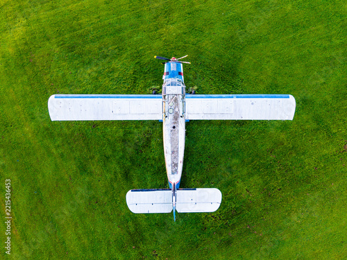 Aerial view of a small propeller plane parked on a vibrant green grass field in Latvia.