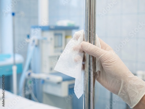 Gloved hand disinfecting stainless steel medical pole in hospital room