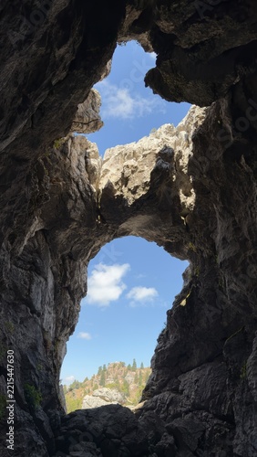 Natural rock arch and cave opening overlooking forest landscape in Gidengelmez Mountains