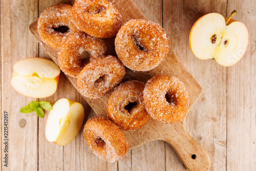 fresh homemade apple cider donuts sprinkled with sugar on wooden board with fresh apple slices