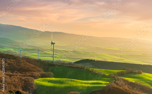 wind turbines of wind power plant producing electricity on green sunset hills on background of landscape. Concept of green energy and environment