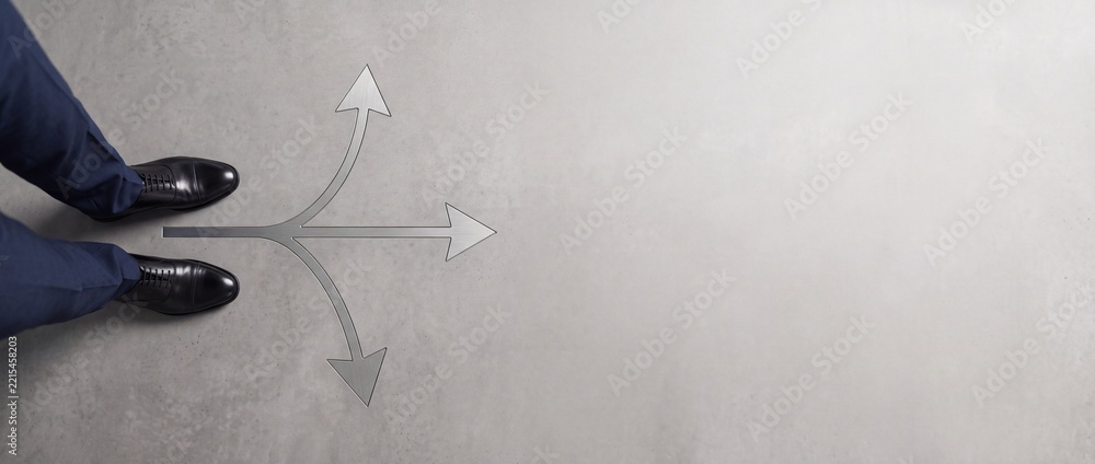 Fototapeta premium High angle view of businessman feet in formal shoes standing before three directional arrows on concrete floor representing career choice and decision making with copy space on the right.