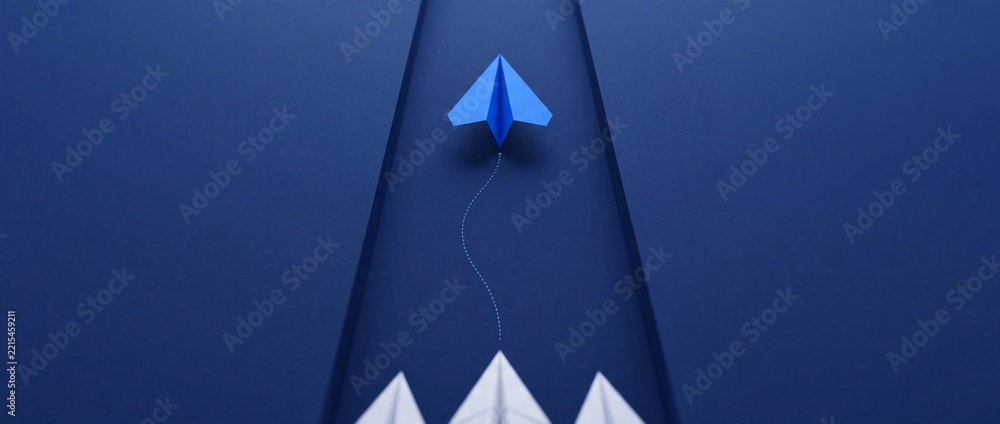 Fototapeta premium Innovative blue paper plane flying ahead of a group of white planes on a blue background, representing leadership, vision, career growth, and unique business strategy with perspective shift.