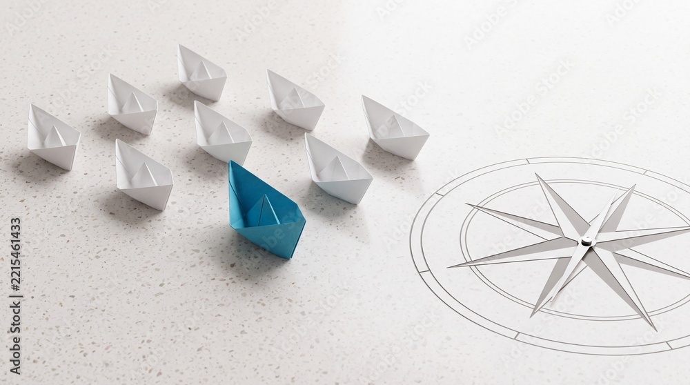 Fototapeta premium A single blue paper boat leading a fleet of white origami boats towards a compass rose symbol on a textured surface, representing leadership, vision, strategic direction, and business success.
