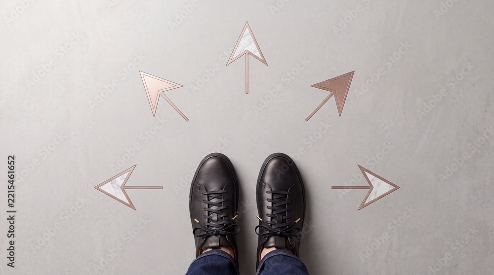 Fototapeta premium Overhead View of Person in Black Leather Sneakers Standing on Concrete Floor with Multiple Metallic Rose Gold Arrows Pointing in Different Directions, Concept of Decision Making and Choosing Path