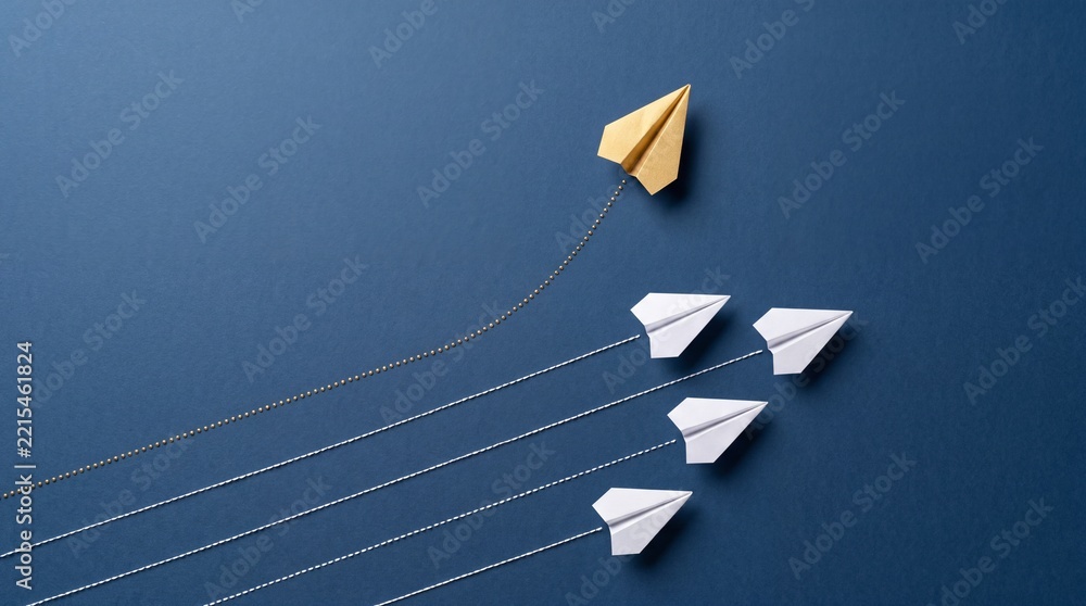 Fototapeta premium Unique Golden Paper Plane Changing Direction From Group of White Ones on Blue Background, Concept of Leadership, Innovation, Individual Success, and Creative Business Strategy Top View Overhead