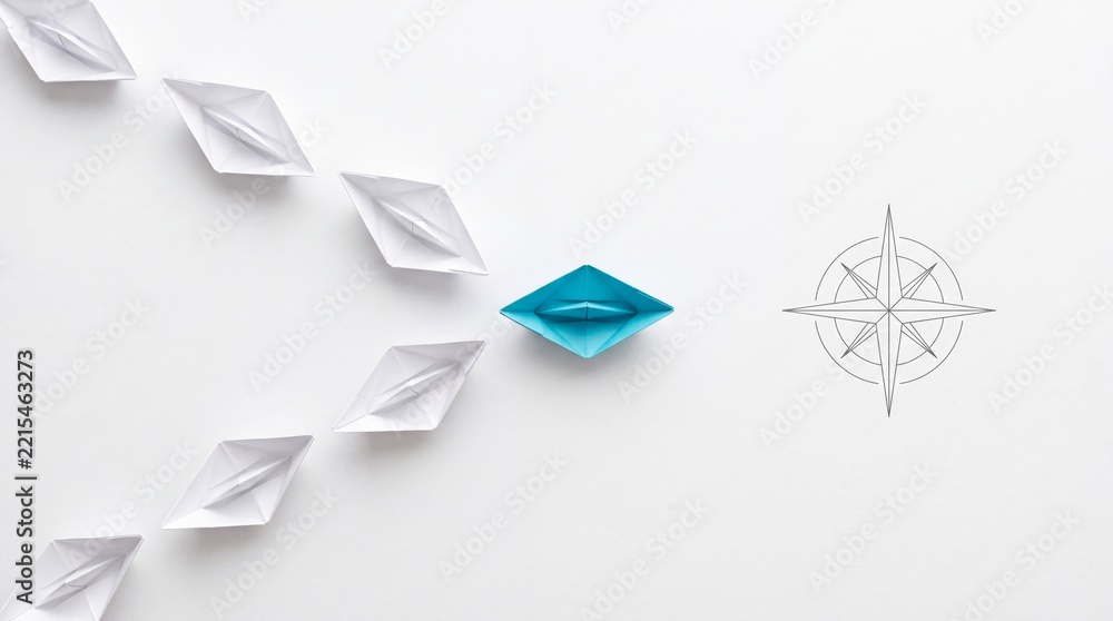 Fototapeta premium Top down overhead view of a blue paper boat leading a group of white paper boats towards a compass icon on a white background, representing leadership, guidance, business strategy and direction