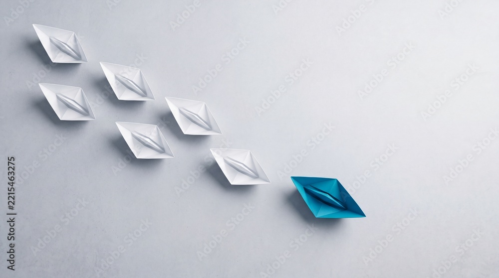 Fototapeta premium Leadership and Business Success Concept with a Blue Paper Boat Leading White Ones in a Top Down View, Symbolizing Innovation, Uniqueness, and Guiding a Team Towards a Goal on a Gray Background