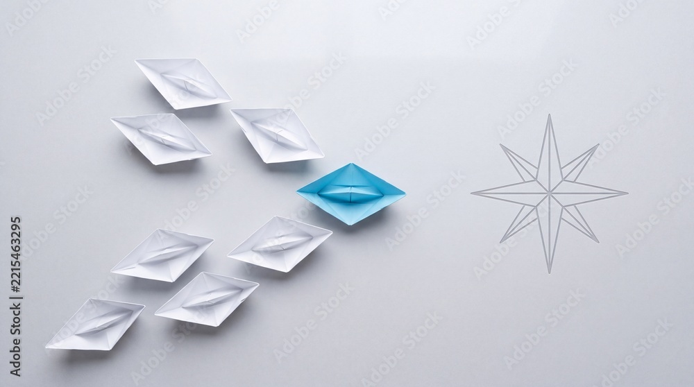 Fototapeta premium Top view of a blue paper boat leading a fleet of white origami boats towards a compass star symbol on a grey background, representing leadership, business vision, and strategic direction.