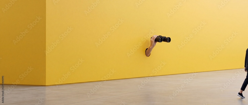 Fototapeta premium Surreal Conceptual Image of a Hand Emerging from a Hole in a Bright Yellow Minimalist Wall Holding Binoculars to Observe or Spy on a Passing Person in a Modern Minimalist Interior Space