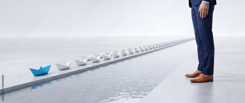 Fototapeta premium Business Leadership and Unique Vision Concept with a Single Blue Paper Boat Leading a Long Row of White Origami Boats on a Narrow Water Channel While a Professional Businessman Stands Nearby