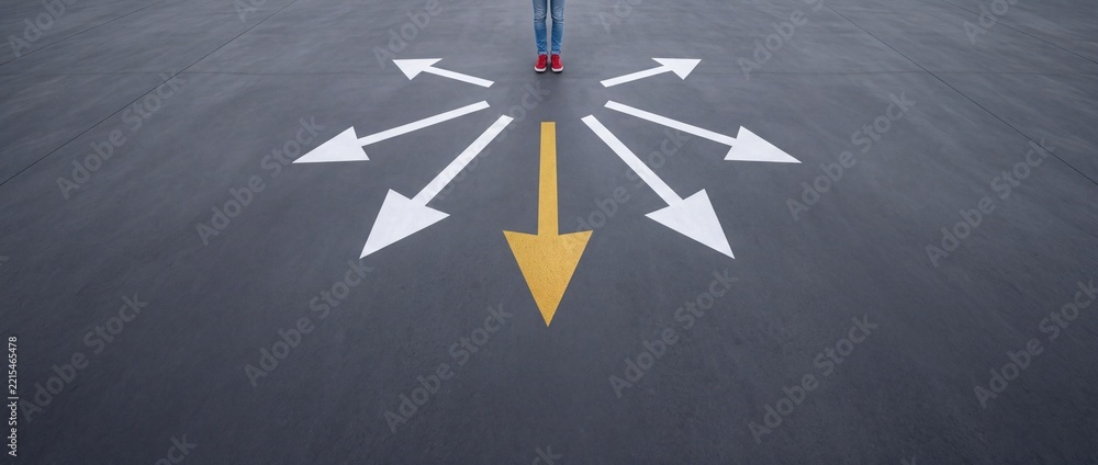 Fototapeta premium Person in Red Sneakers Standing at a Crossroads on Asphalt Surface with Multiple White and One Yellow Directional Arrows Representing Life Choices, Career Decisions, Strategy and New Opportunities