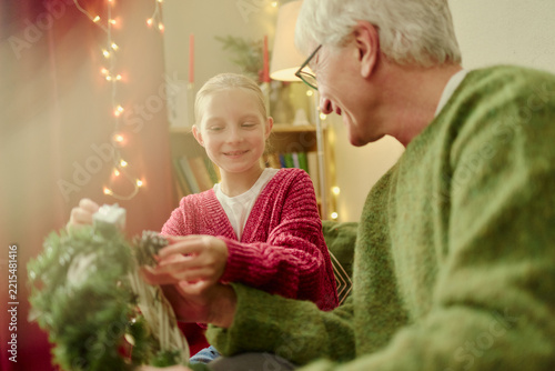 Caucasian senior man and granddaughter decorating holiday wreath together. Concept representing family bonding, suitable for winter marketing campaigns