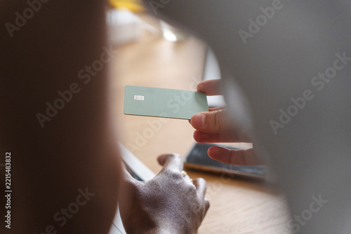 A person sitting at a desk holds up a green payment card to show someone else in a bright office space. They are managing personal finances during a workday.