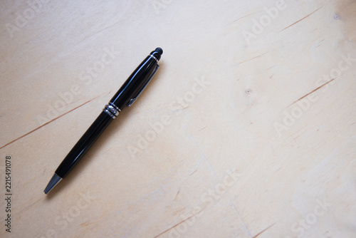 Black glossy pen resting diagonally on light wood tabletop left third, showing stylus tip