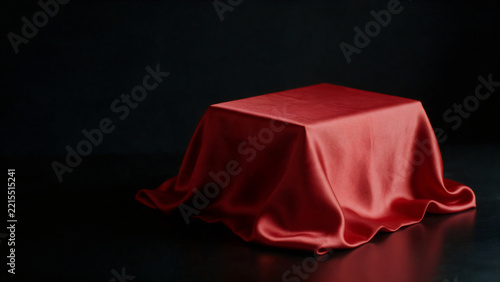 Red satin cloth draped over block pedestal on black background