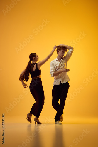 Bachata leader guides partner through energetic turn in orange studio with joyful rhythm. Latin choreography, dynamic motion and partner trust concept.