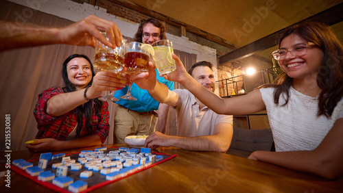 Joyful friends toast above Mahjong tiles after successful round at home. Shared victory, friendly competition and game night concept.