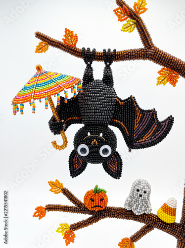 Beaded bat hanging upside down on autumn branch with umbrella