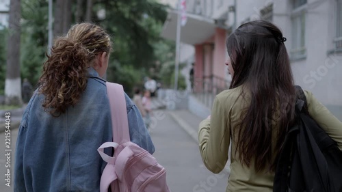 Two young students walking towards a school building entrance on a bright autumn morning outdoors