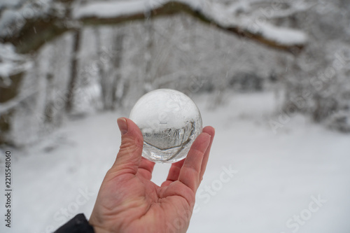 A hand holds a glass sphere reflecting a winter landscape.