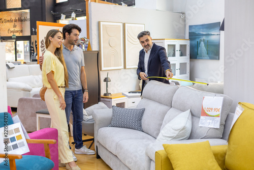 Salesman measuring sofa for young couple in store