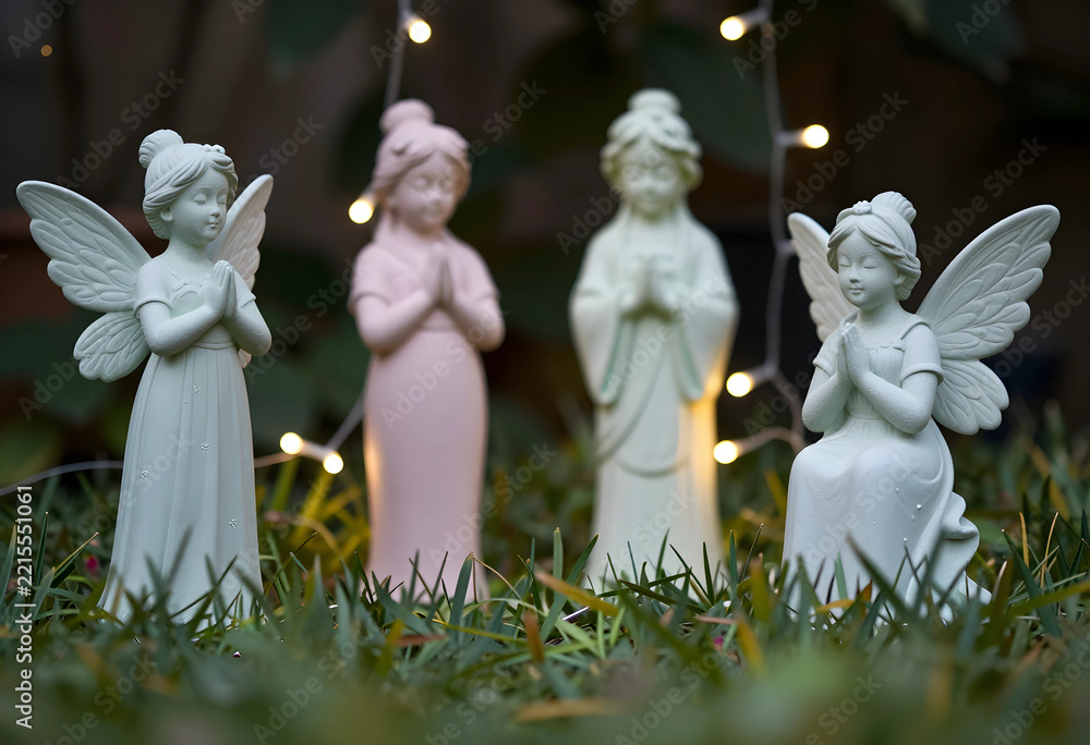 Fototapeta premium Spirituality and mindfulness group of angel figurines praying in a garden with soft fairy lights for peace hope and meditation in nature setting