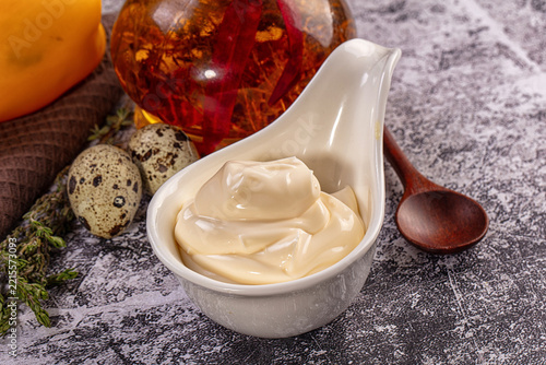 Creamy mayonnaise sauce in white ceramic bowl with quail eggs and infused oil on stone table background