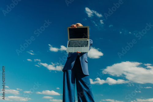 Businesswoman in formal blue suit with laptop against blue sky, low angle view