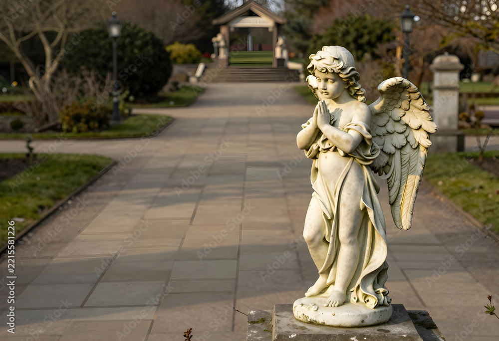 Fototapeta premium Spirituality and peace, stone angel statue praying in a quiet memorial garden with soft sunlight and blurred pathway in the background