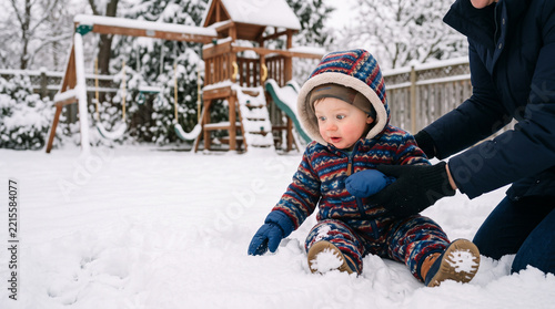 Toddler experiencing first snow in winter backyard with parent support