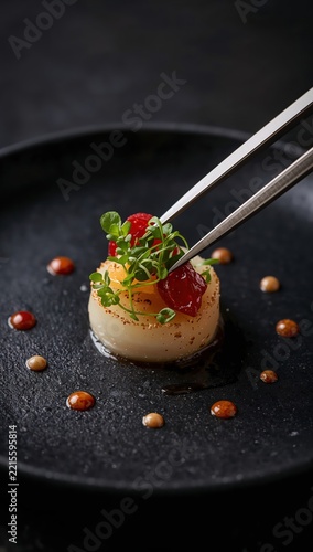 Chef plating modern fusion dish with tweezers microgreens and artistic sauce dots