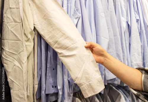 man holding the sleeve of a shirt in a row of shirts, choosing clothes, formal clothes