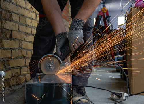 Close-up of a worker cutting a square galvanized ventilation pipe with an angle grinder