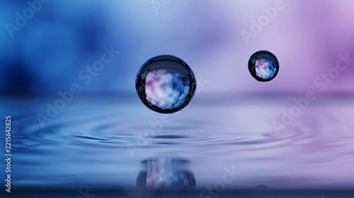 Crystal clear water droplet splashing into calm liquid surface creating ripples in slow motion video footage