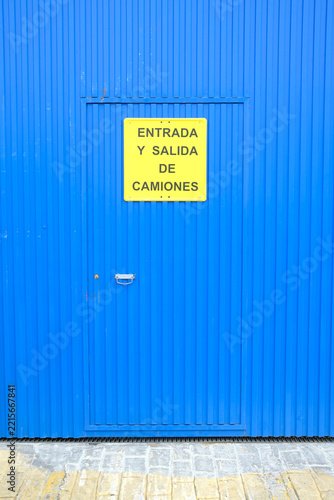 Minimalist blue corrugated metal wall with door and yellow truck entrance sign